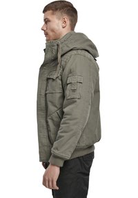 Olivgrüne Bomberjacke mit großer Kapuze, Frontreißverschluss, mehreren Taschen, gerippten Bündchen und glattem Baumwollstoff.