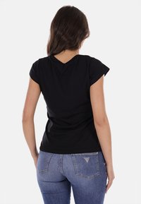 T-shirt nera a maniche corte con scollo a V, aderente in vita, abbinata a jeans blu con un dettaglio a tasca posteriore triangolare.