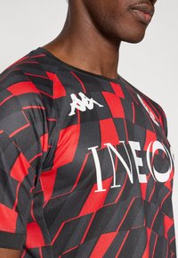 Čierne a červeno vzorované športové tričko s okrúhlym výstrihom, vybavené bielym logom a kontrastnými textúrami v dizajne.