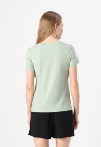 T-shirt vert clair à manches courtes en coton doux. Encolure ronde et coupe simple, associé à un short noir.