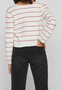 Biały sweter dziany z czerwonymi poziomymi paskami, zestawiony z czarnymi dżinsami. Sweter ma szeroki dekolt i ściągacze na mankietach.