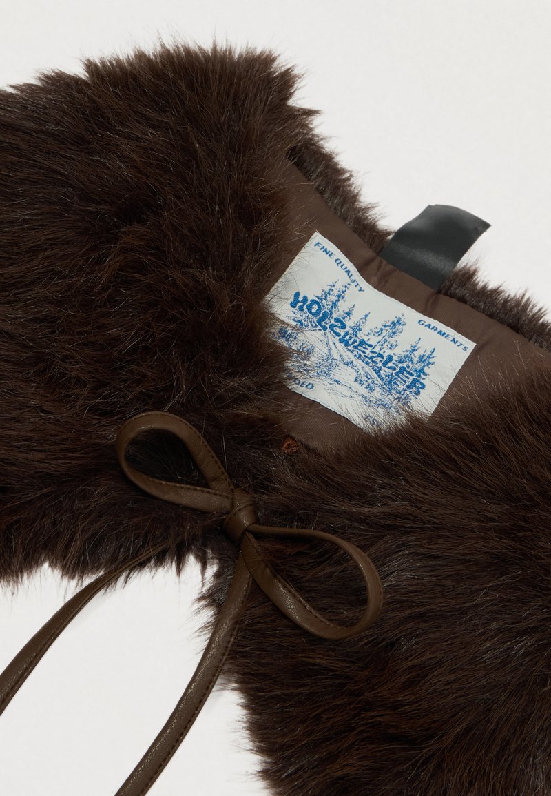Brown fur garment with a soft texture, featuring a bow-shaped leather tie and a sewn-in label depicting trees and "Wool Sweater."