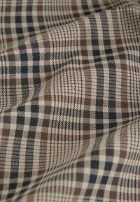 Gros plan d'un tissu froissé avec un motif à carreaux beige, marron et noir.