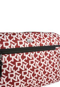 Bolsa de tela roja con un patrón de logotipos blancos en repetición. Cremallera negra con una etiqueta de metal de marca. Textura suave, forma rectangular.