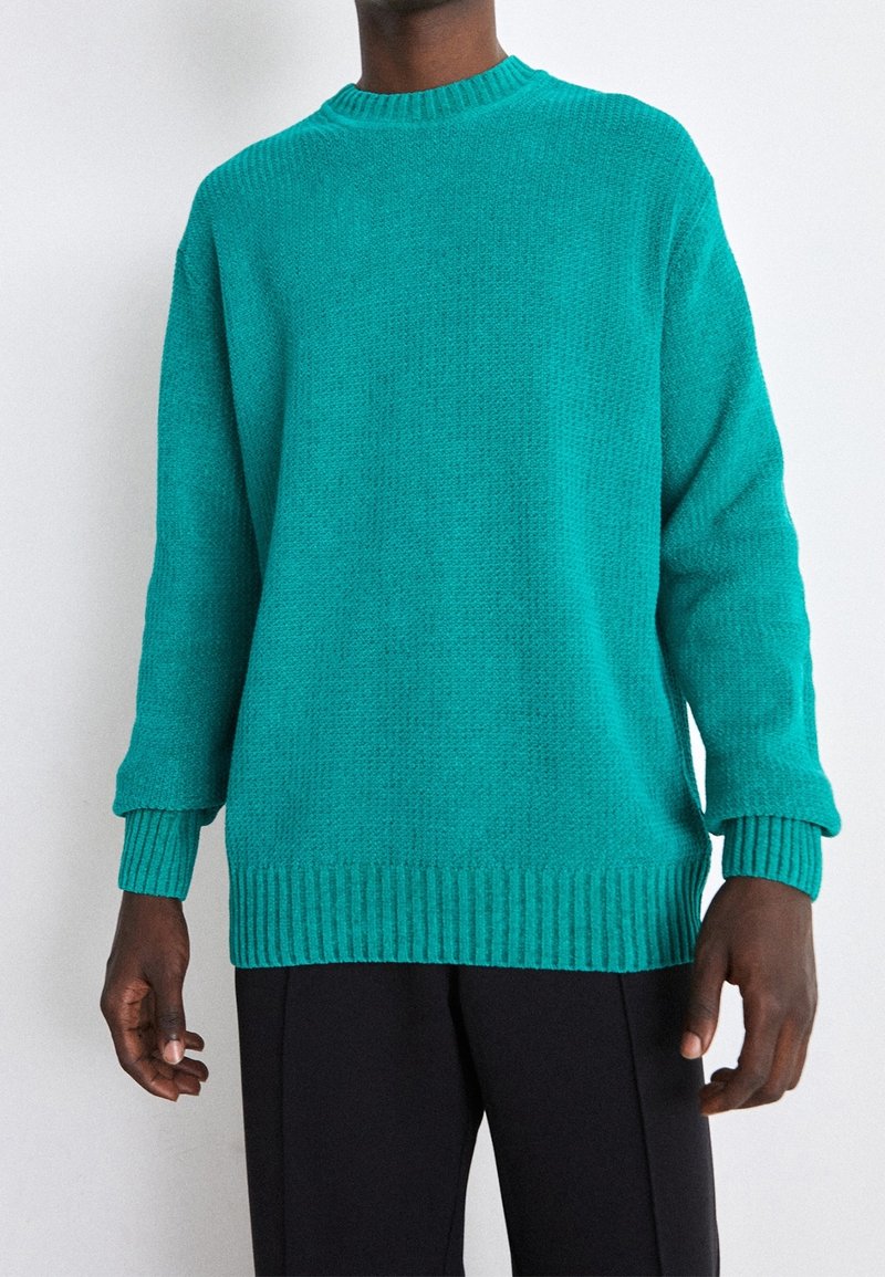 Turkos stickad tröja med rund halsringning, ribbade ärmslut och nederkant. Tillverkad av strukturerad tyg, med långa ärmar och en oversized passform.