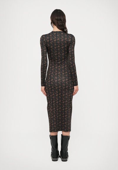 Φόρεμα με μακριά μανίκια, εφαρμοστό, σε μαύρο χρώμα με καφέ αφηρημένο σχέδιο. Το μήκος φτάνει μέχρι τη μέση της γάμπας και συνδυάζεται με μαύρες μπότες μέχρι το γόνατο.