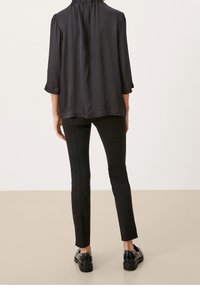 Czarna, lekka bluzka z rękawami 3/4 i marszczonym dekoltem, zestawiona z dopasowanymi czarnymi spodniami i błyszczącymi butami, widziana od tyłu.