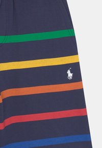 Tmavě modré tričko s vodorovnými pruhy v zelené, žluté, oranžové, červené a modré barvě; obsahuje malý bílý motiv hráče póla.