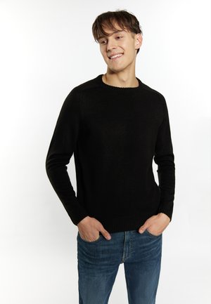 Schwarzer Strickpullover mit Rundhalsausschnitt, gerippten Bündchen und Saum. Getragen mit blauen Jeans, die einen figurbetonten, aber dennoch bequemen Stil zeigen.