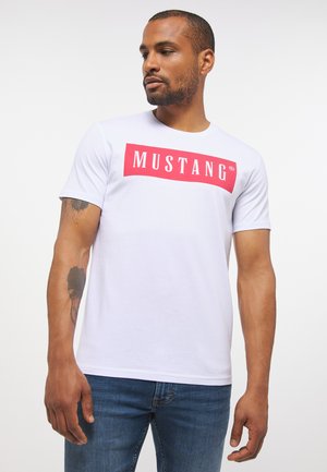 Biała koszulka z okrągłym dekoltem, wykonana z bawełny, z wyraźnym czerwonym prostokątnym graficznym motywem z napisem "MUSTANG". Miękka tekstura, krótkie rękawy.