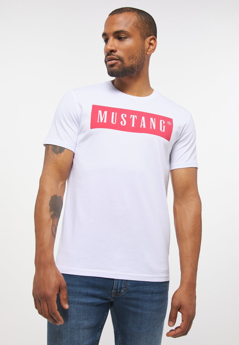 Biała koszulka z okrągłym dekoltem, wykonana z bawełny, z wyraźnym czerwonym prostokątnym graficznym motywem z napisem "MUSTANG". Miękka tekstura, krótkie rękawy.