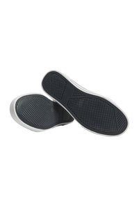 Czarne gumowe podeszwy butów z wzorzystą fakturą, z białymi akcentami po bokach i gładkim brzegiem. Uformowane dla wygody i przyczepności.