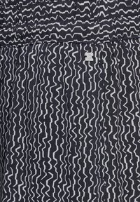 Tissu à motif zigzag noir et blanc avec un léger éclat, doté d'une taille élastique et d'une petite étiquette de logo intégrée dans le design.