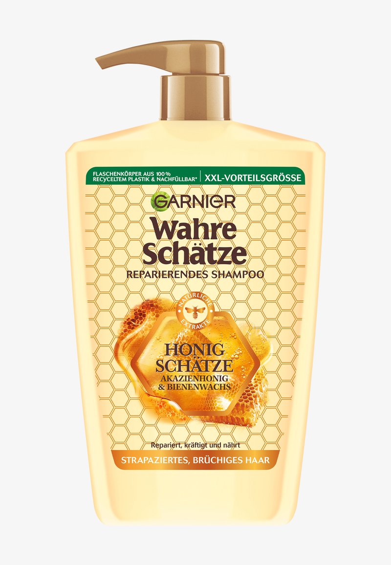 Bottiglia color miele con un tappo a pompa, caratterizzata da un motivo a nido d'ape e etichette nere e verdi, indicante shampoo per la riparazione dei capelli danneggiati.