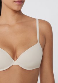 Beiger gepolsterter BH mit verstellbaren Trägern, glatter Textur, tiefem Ausschnitt und nahtlosem Design für einen minimalistischen Look.