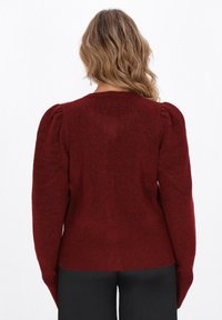 Maglione rosso lavorato a maglia con maniche lunghe a spalla a sbuffo e orlo a costine. Texture morbida con una silhouette aderente.