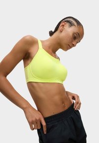 Ljus neon-gul sport-bh med justerbara band, slät textur och ventilerad underdel, tillsammans med svarta träningsshorts.