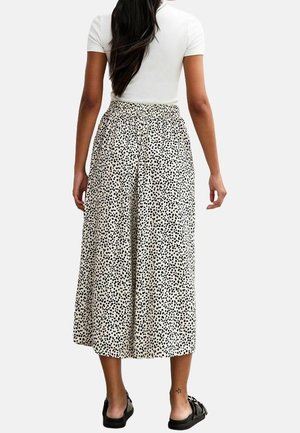 Jupe midi avec un motif à pois noir et blanc, taille élastique, tissu fluide et coupe ample ; associée à un top blanc ajusté.