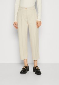 Beige tailored trousers with a straight leg, featuring a front button closure, subtle crease, and pockets, paired with black loafers.