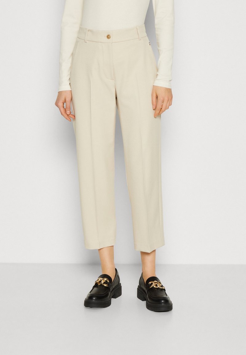 Beige tailored trousers with a straight leg, featuring a front button closure, subtle crease, and pockets, paired with black loafers.