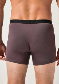 Boxer shorts para hombre burdeos con una cinturilla elástica negra. La tela parece suave con un diseño ajustado que termina a mitad del muslo.