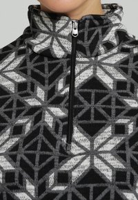 Fleece-Pullover mit hohem Kragen, ausgestattet mit einem schwarz-weißen geometrischen Muster, einem vorderen Reißverschluss und einer weichen Strickstruktur.