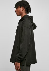 Svart oversized hettegenser laget av bomull, med en frontlomme, snøring i hetten og sidespalter. Glatt tekstur med en avslappet passform.