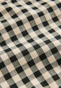 Crno-bež karirani materijal s uzorkom mreže koji se sastoji od izmjeničnih kvadrata, izrađen od teksturiranog materijala.