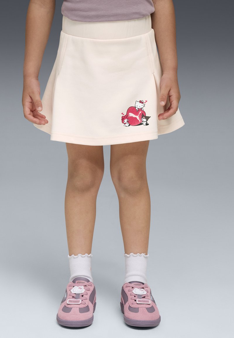Falda en forma de A color melocotón con una textura suave, que presenta un gráfico colorido de gatos y un corazón en la parte frontal. Se lleva con zapatillas rosas.