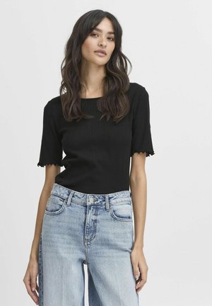 Haut en maille noire côtelée à manches courtes avec des bords festonnés, associé à un jean taille haute en denim bleu clair.
