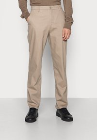 Chino beige con vestibilità dritta, dotati di tasche laterali e una texture in cotone morbida. Abbinati a sneakers nere.