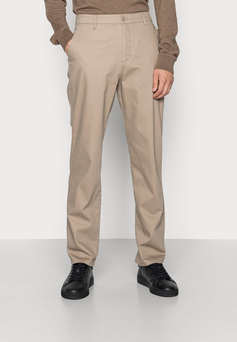 Chino beige con vestibilità dritta, dotati di tasche laterali e una texture in cotone morbida. Abbinati a sneakers nere.