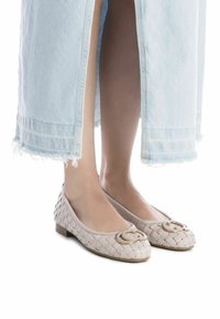 Ballerine intrecciate beige chiaro con un'accenno di logo dorato, tacco basso a blocco e punte arrotondate, abbinate a una gonna in denim sfrangiata.