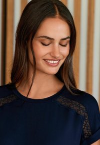 Navy blue top with lace accents on shoulders, round neckline, soft texture, and short sleeves. Smooth fabric complements delicate lace.