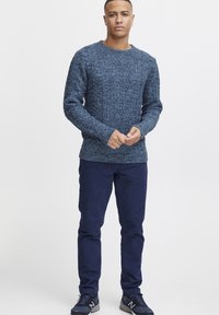 Pulover tricotat de culoare albastru închis cu un model texturat, guler rotund și manșete dantele. Asortat cu pantaloni de culoare albastru marin și încălțăminte sport.