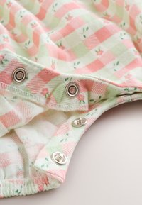 Boutons-pression sur tissu écossais rose et vert avec petits motifs floraux, partie d'une ouverture de vêtement doux.