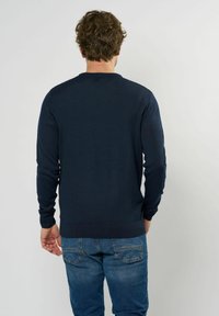 Dunkelblauer Strickpullover mit strukturiertem Muster, Rundhalsausschnitt und gerippten Bündchen und Saum, getragen mit blauen Jeans.
