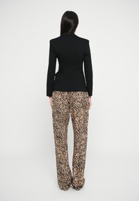 Blazer noir avec des épaules structurées associé à un pantalon large à imprimé léopard. Tissu lisse, jambes larges avec des détails de motif animal.