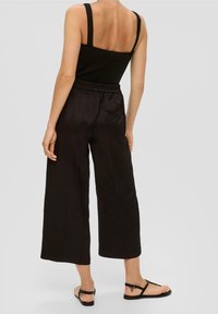Černý top bez rukávů zkombinovaný s černými kalhotami s vysokým pasem a širokými nohavicemi. Hladká tkanina, elastický pas a minimální šití.