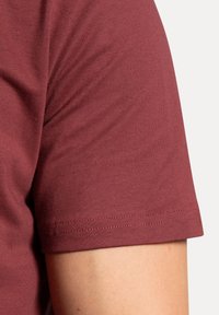 T-shirt corto marrone scuro con texture liscia e forma aderente. Presenta un collo giro standard e un orlo dritto con dettagli di cucitura.