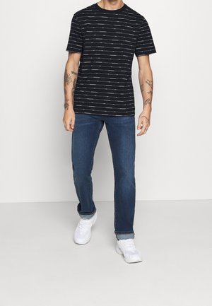 Camiseta negra de manga corta con rayas horizontales blancas, combinada con jeans azules y zapatillas blancas. La tela parece suave y tiene un ajuste casual.