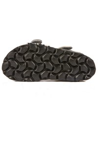 Semelle de chaussure en caoutchouc noir avec un motif en vagues, présentant des rainures pour la traction et une petite sangle latérale pour l'ajustement.