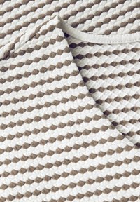 Bomullstyg med en strukturerad, mönstrad design som har växlande bruna och vita skinn. Kant har en slät, vit kant.