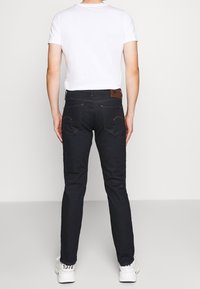 Jeans de mezclilla azul oscuro con un corte slim, bolsillos traseros y detalles de costura en contraste, combinados con una camiseta blanca de manga corta.
