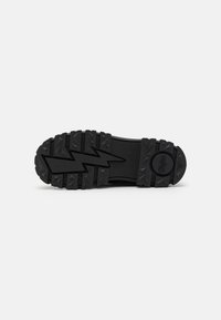 Suola di scarpa in gomma nera con profonde scanalature e un motivo a zigzag per la presa, caratterizzata da un logo circolare sul lato del tallone per il branding.