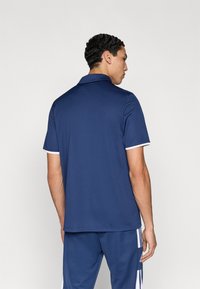 Μπλε μπλουζάκι πόλο με γιακά και λευκή λεπτομέρεια στα μανίκια, κατασκευασμένο από απαλό και ελαφρύ ύφασμα. Φοριέται με αντίστοιχο μπλε παντελόνι.