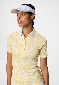 Koszulka polo z krótkim rękawem w jasnym żółtym kolorze z falistym wzorem. Posiada klasyczny kołnierzyk oraz subtelne logo na piersi.
