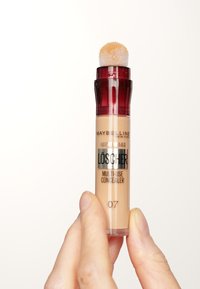 Maybelline Mehrzweck-Concealer in einem klaren Röhrchen mit rotem Deckel, Schwammapplikator und flüssigem hellbeige. Das Etikett trägt die Aufschrift "Löscher 07."