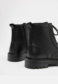 Bottines en cuir noir à texture lisse, avec une fermeture éclair latérale et une semelle robuste en caoutchouc crantée. Équipées d'une languette arrière pour un enfilage facile.