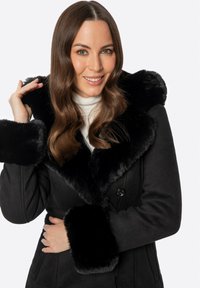 Czarny płaszcz z miękkim, sztucznym futrzanym kołnierzem i mankietami. Posiada podwójne zapięcie na guziki i teksturowaną tkaninę. Gładka podszewka wewnętrzna.